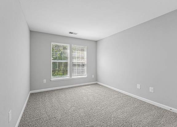 A room with a window and a carpeted floor.
